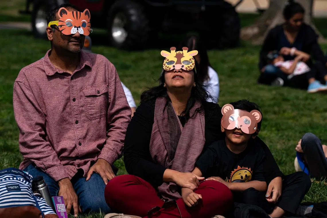 Nishant Signal, Song Singal and Ivan Signal of Sterling, VA, looking up at the solar eclipse with their home modified eclipse glasses on April 8, 2024, in Washington, DC. 