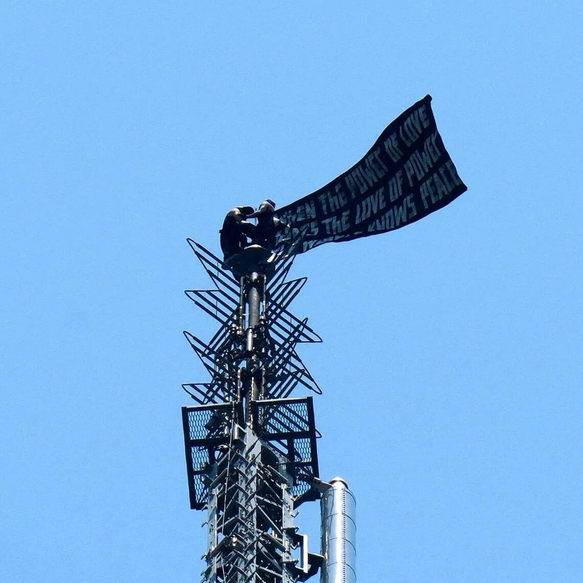 The pair, dressed in sleeveless black outfits, hung onto the landmark skyscraper’s antenna - 443m above ground - and unfurled a banner urging world peace.