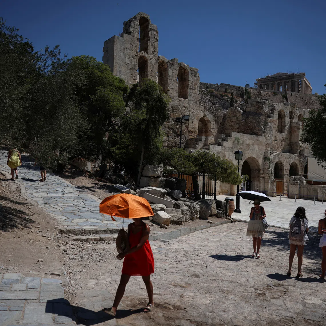 People seeking shade under umbrellas while visiting the Herodes Atticus Theatre under the Acropolis in Athens in July. Most theatres were closed in Greece on Dec 27.