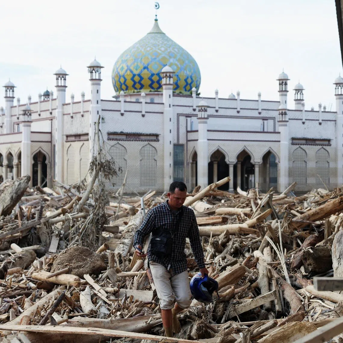 A survivor walks through tree trunks stranded at a mosque in an area affected by a deadly flash flood following heavy rains in Aceh Tamiang, Indonesia. 