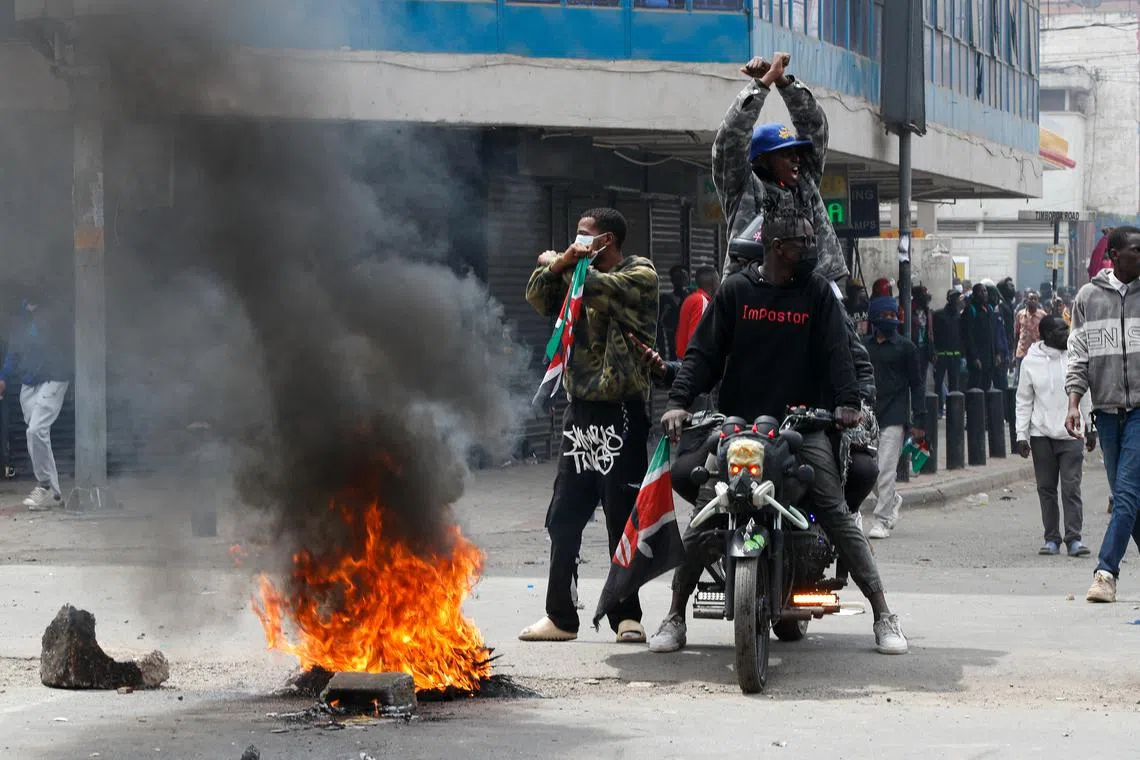 Men sit on a motorcycle next to a fire burning, during a demonstration over police killings of people protesting against the imposition of tax hikes by the government, in Nairobi, Kenya, July 2, 2024. REUTERS/Monicah Mwangi/File Photo