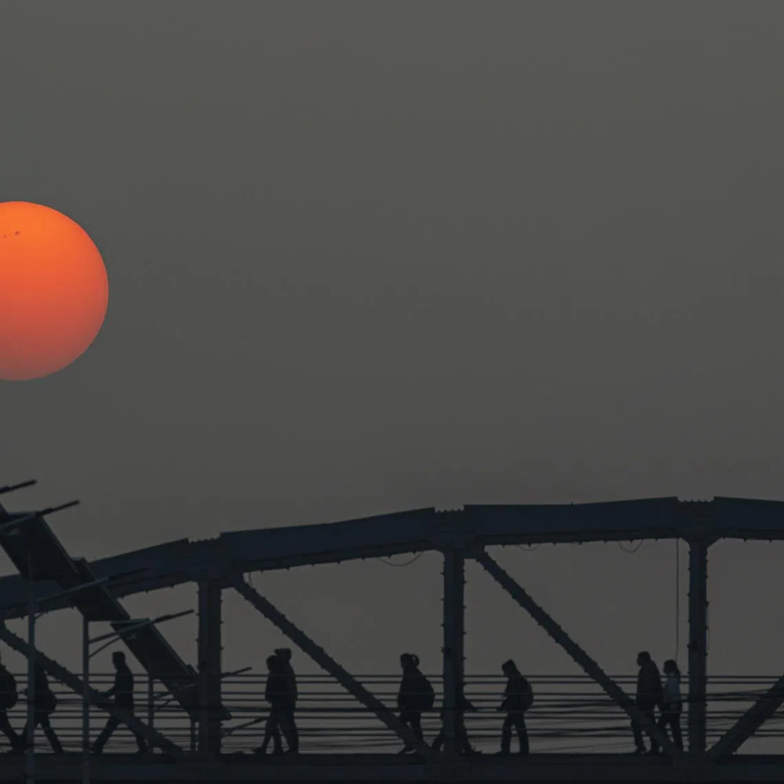 People cross a pedestrian bridge as the sun rises in Kathmandu on Feb 28, 2023.
