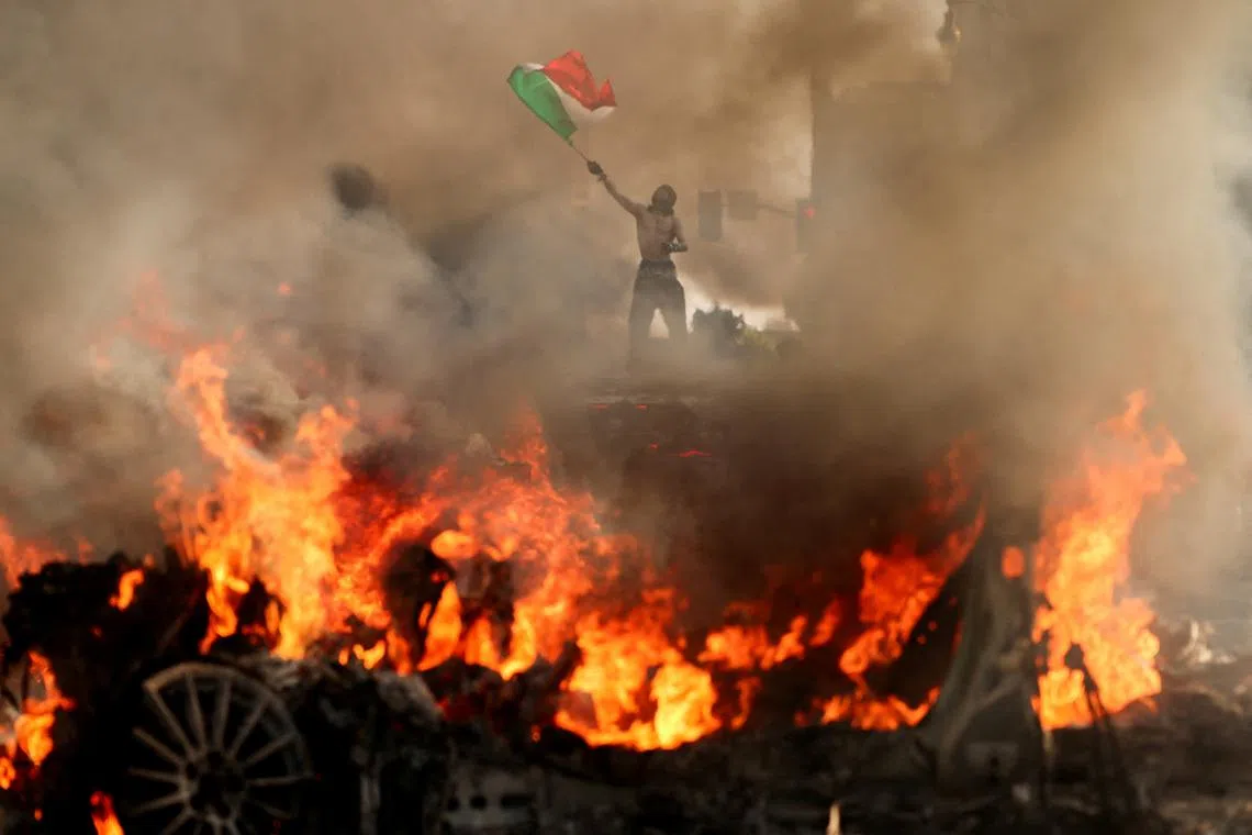 A man waving a Mexican flag as smoke and flames rise from a burning vehicle during a protest against federal immigration sweeps, near Los Angeles City Hall in downtown Los Angeles, California, US, on June 8, 2025. 