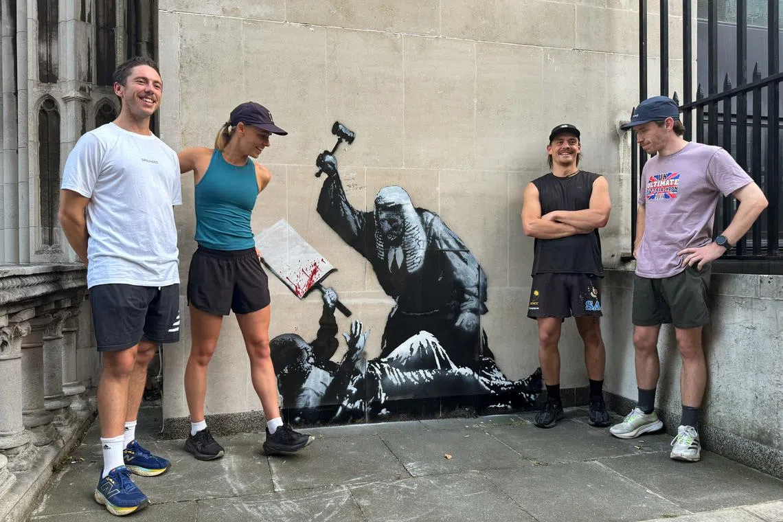 People react in front of a new mural by anonymous artist Banksy on the Royal Courts of Justice in London, on Sept 8.