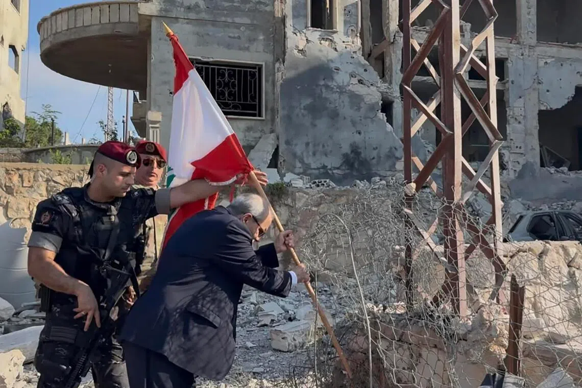 Lebanese Prime Minister Nawaf Salam placing a national flag along a damaged street in the southern village of Zawtar al-Gharbiya on July 22.