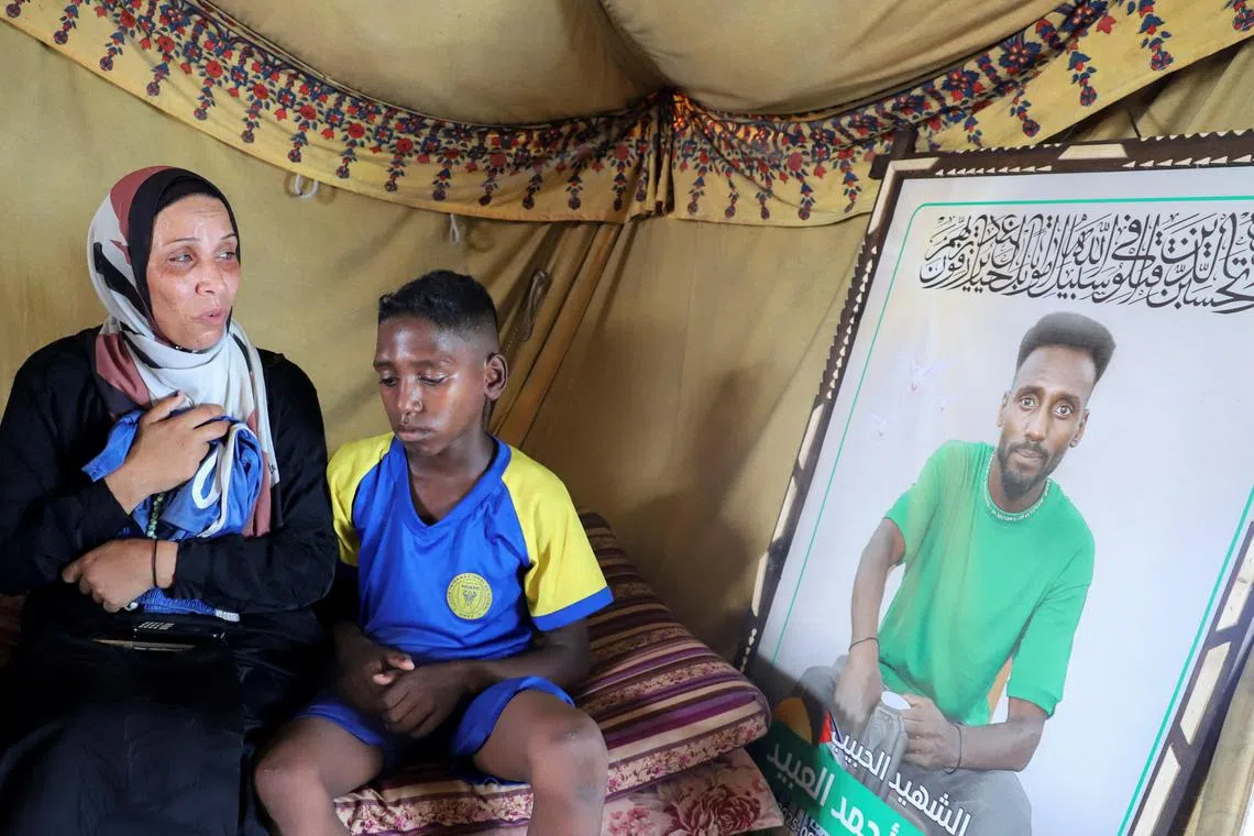 Doaa, the widow of late footballer Suleiman Al-Obeid, known as the "Palestinian Pele," who was killed by an Israeli strike targeting people waiting for humanitarian aid, according to the Palestine Football Association, looks at his picture while holding his shorts, as her son sits beside her inside their tent in Gaza City Aug 9, 2025. 