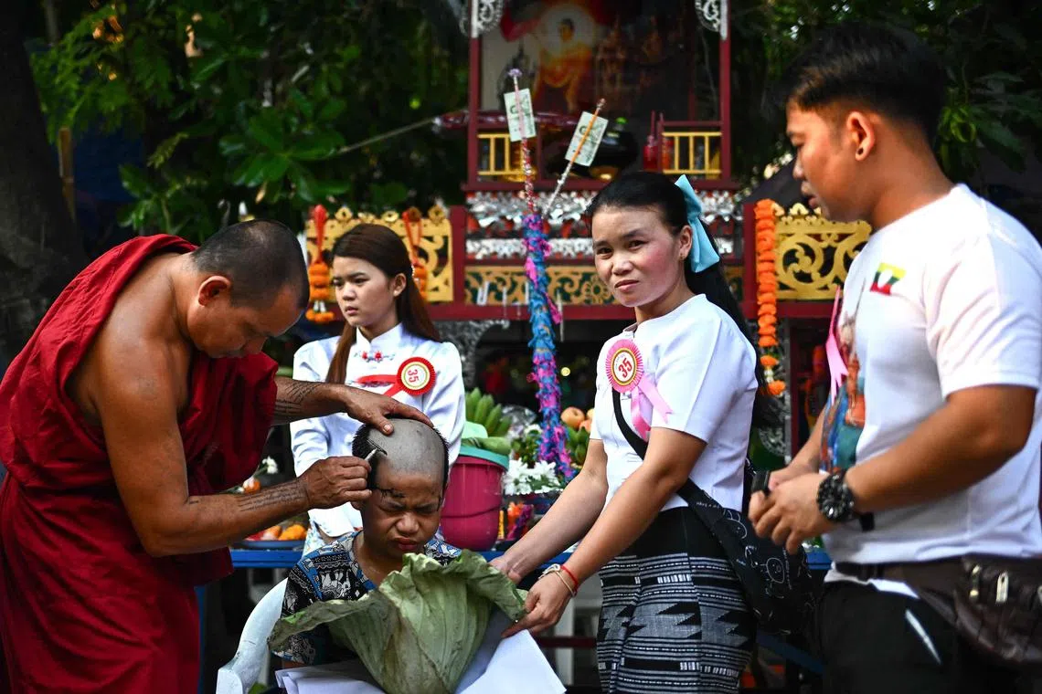 TOPSHOT - This photograph taken on March 27, 2025 shows twelve year-old Saenghan, a young ethnic Shan boy getting his head shaved by a Buddhist monks on the eve of the annual Poy Sang Long procession at Wat Ku Tao Temple in northern Thailand’s Chiang Mai province. Dressed in flowers, finery and makeup, scores of boys were paraded around a temple in Thailand after having their heads shaved -- a symbolic start to a centuries-old Shan monkhood ordination. (Photo by MANAN VATSYAYANA / AFP) / To go with 'THAILAND-MYANMAR-RELIGION-CULTURE-MINORITIES' by Montira RUNGJIRAJITTRANON