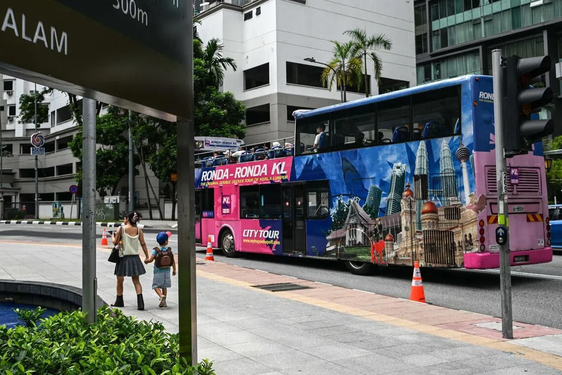 A woman walks with her son as a city tour bus passe by on a street in Kuala Lumpur on May 25, 2025.