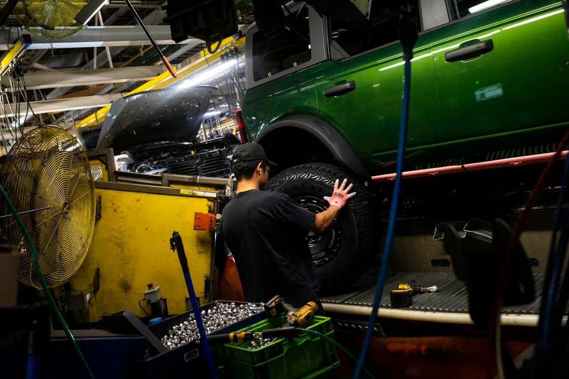 A worker fits a wheel onto a Ford Bronco at the automaker's plant in Wayne, Mich.  US automakers are facing difficult choices.