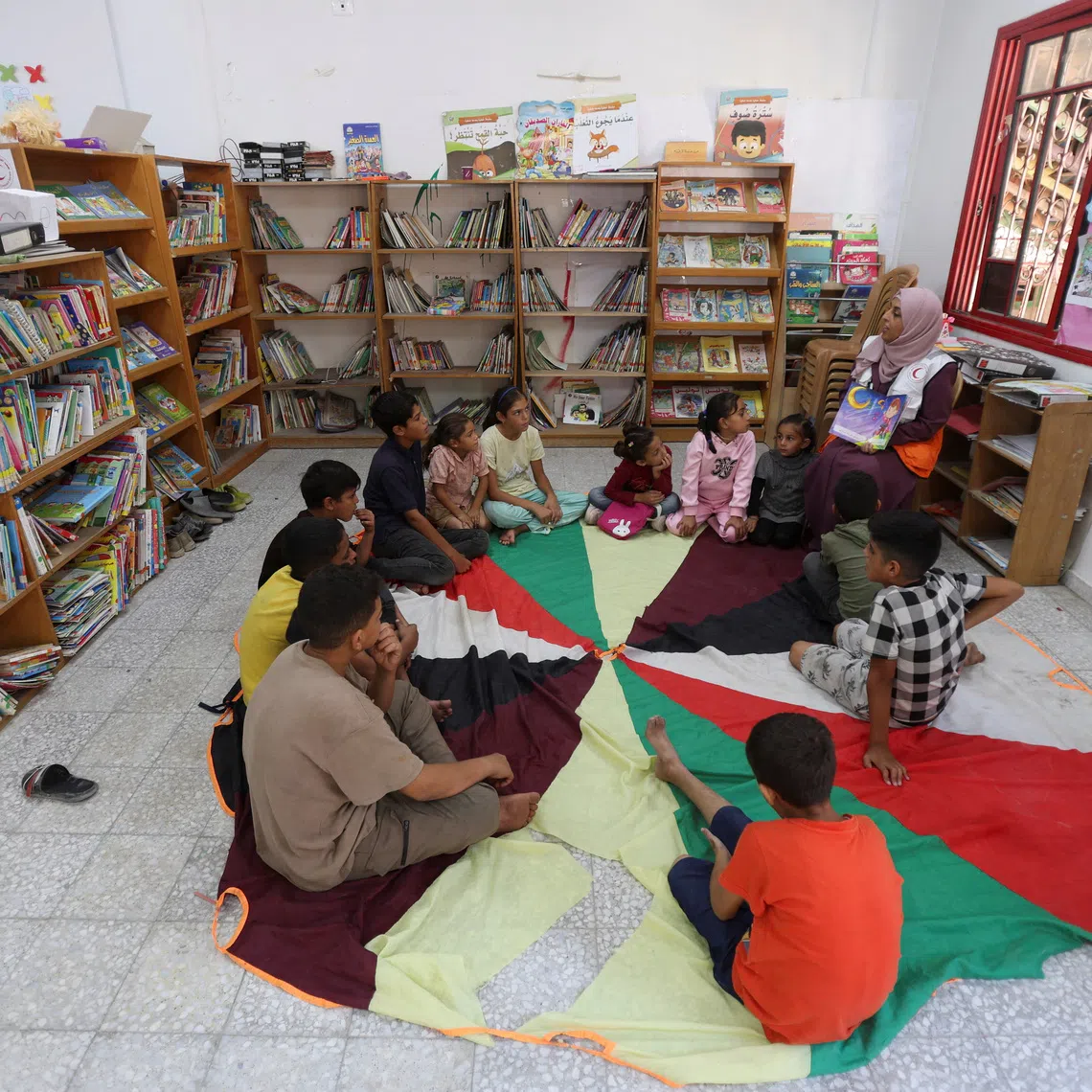 A member of the Palestinian Red Crescent Society reads a story to children as part of mental support activities at the organization’s centre, in Khan Younis in the southern Gaza Strip, October 30, 2025. REUTERS/Ramadan Abed