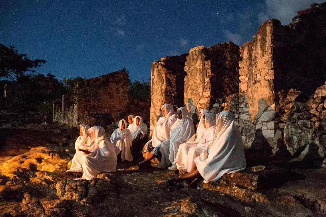 Catholic women dressed in white sheets taking part in the Terno das Almas procession in Igatu, Brazil, on March 26, 2024. Terno das Almas is an ancient ritual that takes place every night during Holy Week when participants make a pilgrimage through various parts of the village, praying and singing for the souls of their dead. 
