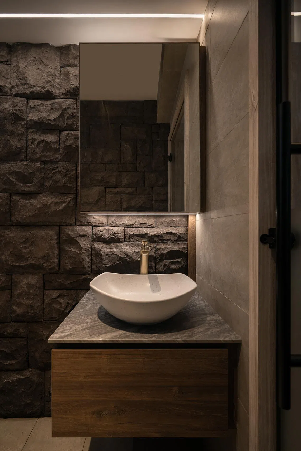 Brushed-gold fittings stand out against the bathroom’s dark stone, while soft lighting highlights the texture.