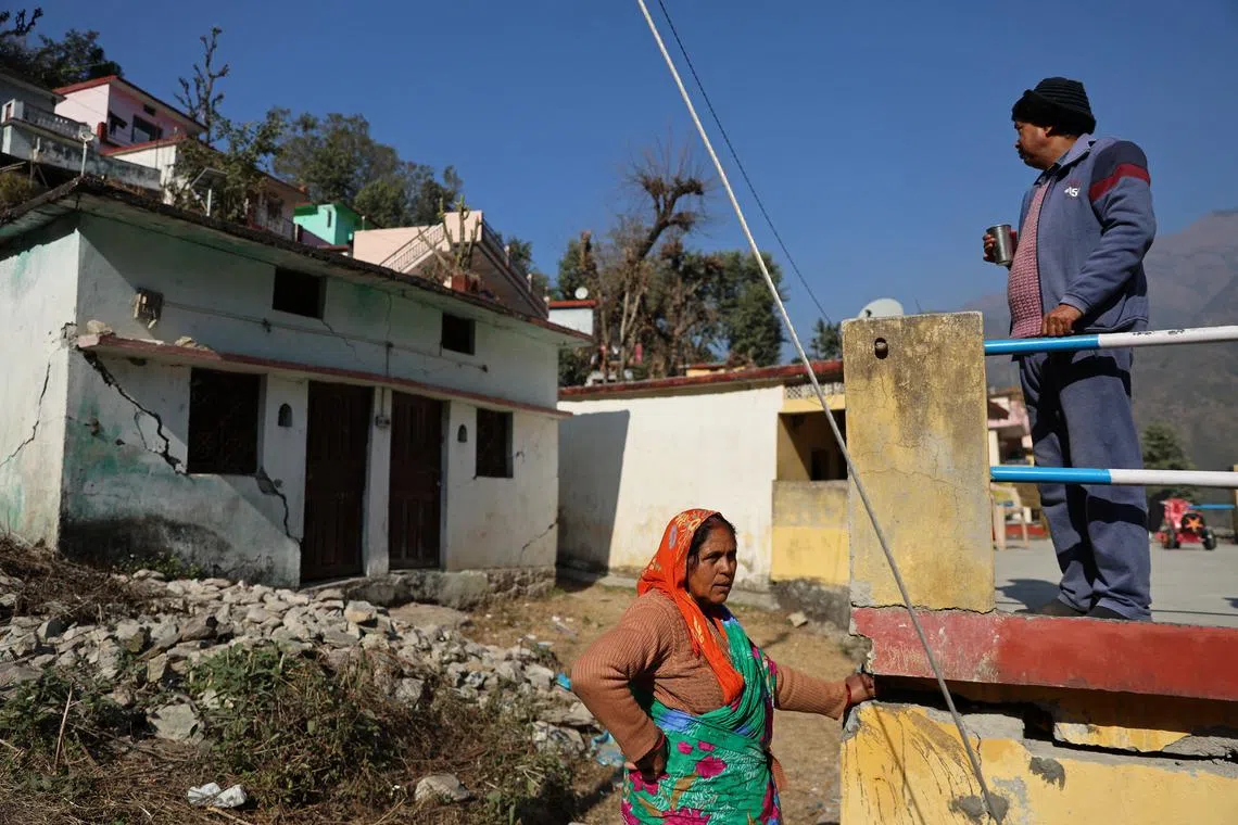Jaswant Singh Butola (R), 55, looks at houses which have been vacated due to damage that he says developed after infrastructure works began close to the village, while standing next to his neighbour Munni Devi, 55, in Maroda, in the northern state of Uttarakhand, India, Jan 17, 2023. "I have been living here for past 40 years," Devi said. "The whole night the work goes on below on the railway line and the cement from the house keeps falling down. We live in a lot of risk."   
