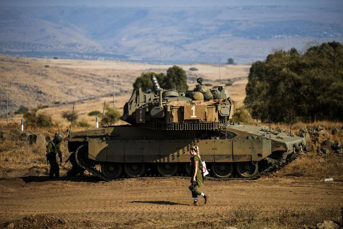 An Israeli soldier walks past a tank amid heightened tensions between Israel and Lebanon, as seen from the border with Lebanon in northern Israel, October 14, 2023. REUTERS/Gil Eliyahu