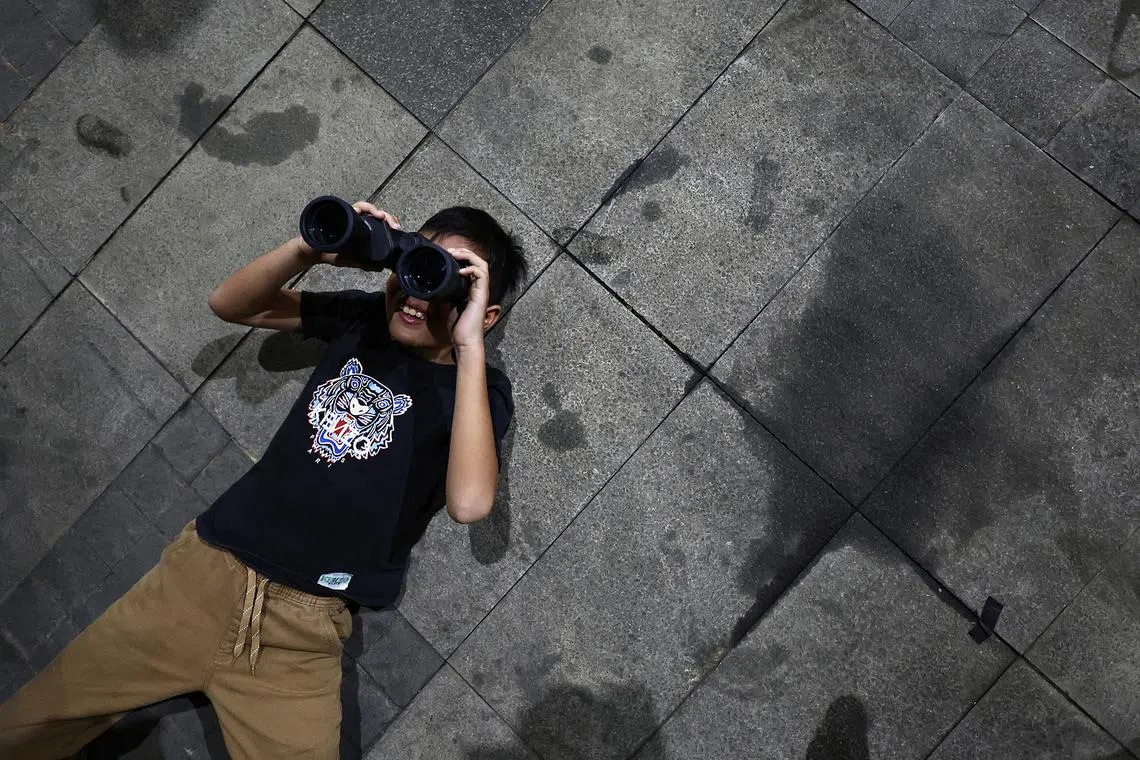 A boy uses binoculars to observe the blood moon during a total lunar eclipse in Jakarta, Indonesia, on Sept 7, 2025. 