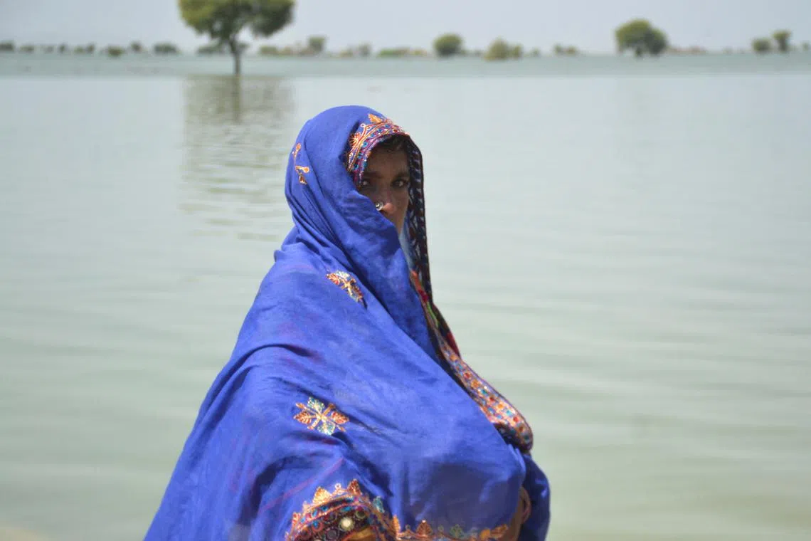 A woman, displaced because of the floods, walks with her belongings covered with scarf, with the flood water in the background, following rains and floods during the monsoon season in Sehwan, Pakistan September 20, 2022. REUTERS/Stringer NO RESALES. NO ARCHIVES.