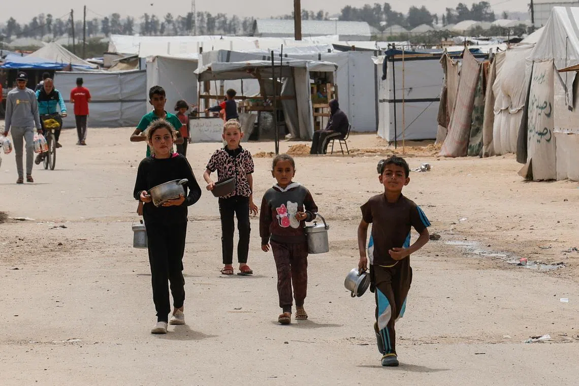 FILE PHOTO: Children walk as Palestinians wait to receive food cooked by a charity kitchen, in Khan Younis, southern Gaza Strip, April 6, 2025. REUTERS/Hatem Khaled/File Photo