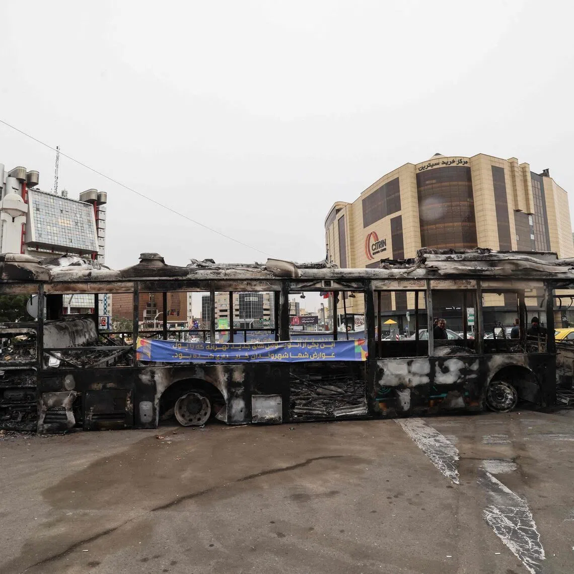 A photograph shows the wreckage of a burnt bus bearing a banner that reads "This was one of Tehran’s new buses that was paid for with the money of the people’s taxes,” in Tehran's Sadeghieh Square on Jan 15, 2026. A protest movement across Iran, initially sparked by economic grievances, has turned into one of the biggest challenges yet to the clerical leadership since it took power in 1979. 