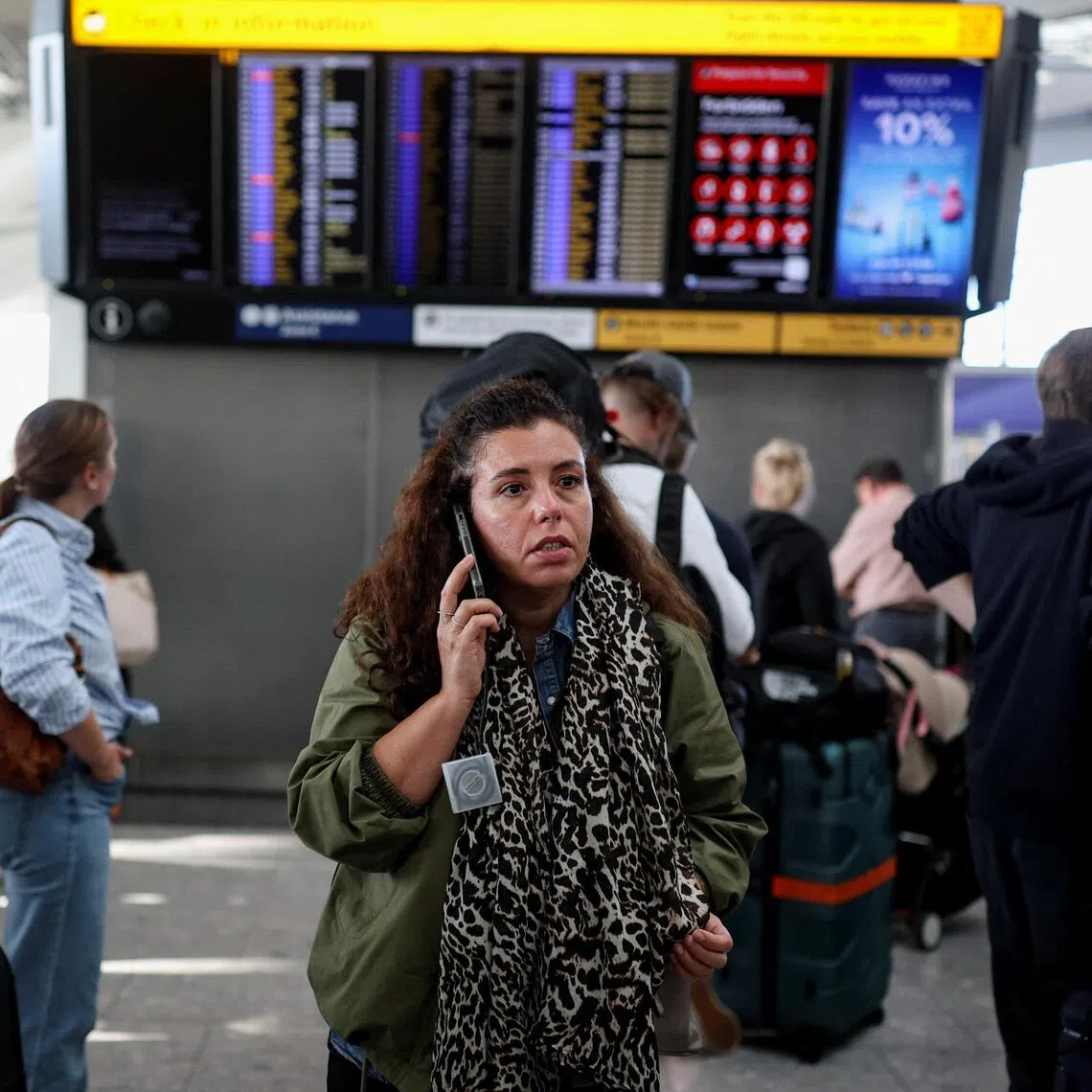 A passenger uses a mobile phone while others look at a departure board displaying cancelled flights at Heathrow Airport’s Terminal 5 in London, Britain, on Sept 8.