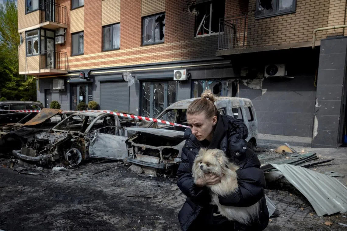 A resident carrying a dog as she runs from an apartment building to avoid falling glass shards after it was damaged during a night of Russian missile and drone strikes, amid Russia's attack on Ukraine, in Shchaslyve, outside Kyiv, Ukraine, May 14.