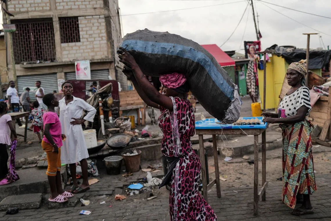 FILE PHOTO: A woman carries sack of charcoal, as she walks down a busy street, in Jamestown in Accra, Ghana  December 6, 2024. REUTERS/Zohra Bensemra/File Photo