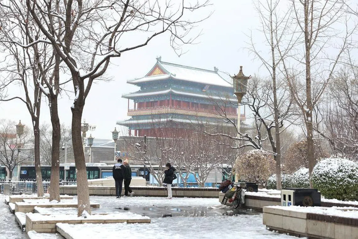 People stand near Qianmen Street on a snowy day in Beijing, China December 11, 2023. REUTERS/Tingshu Wang