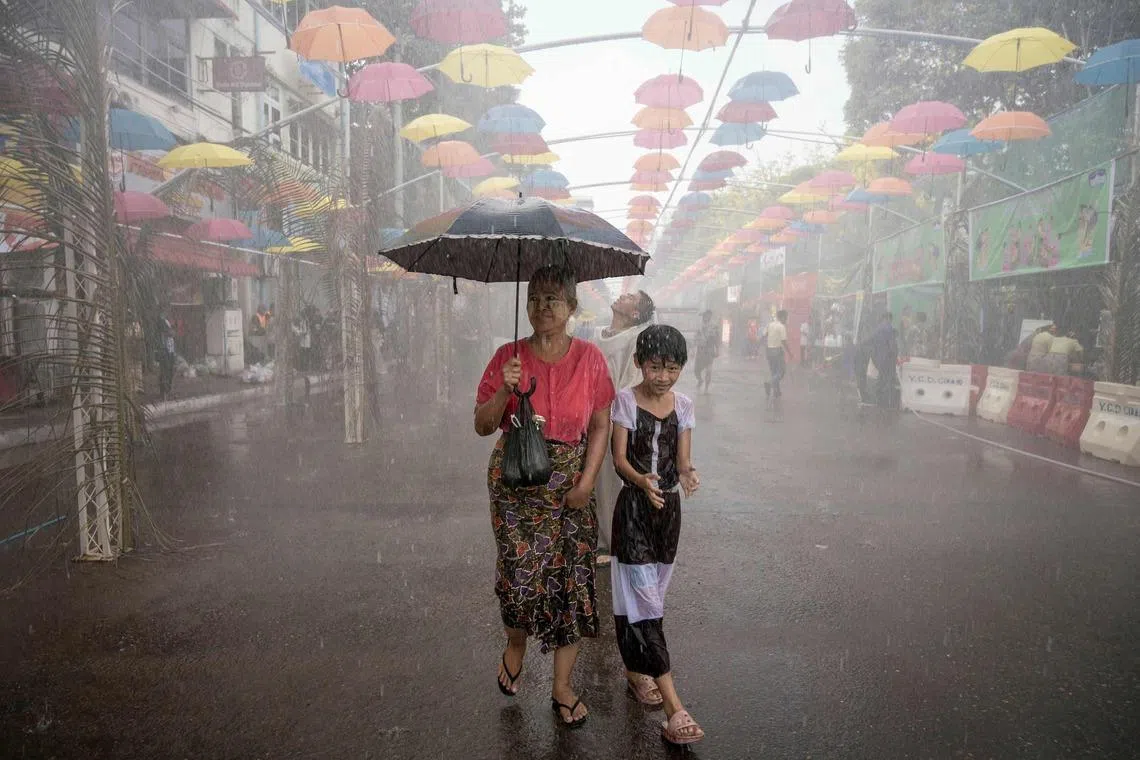 TOPSHOT - People walk under sprinklers during celebrations for Myanmar's Buddhist New Year water festival, also known as Thingyan, in Yangon on April 13, 2026. (Photo by Sai Aung MAIN / AFP)