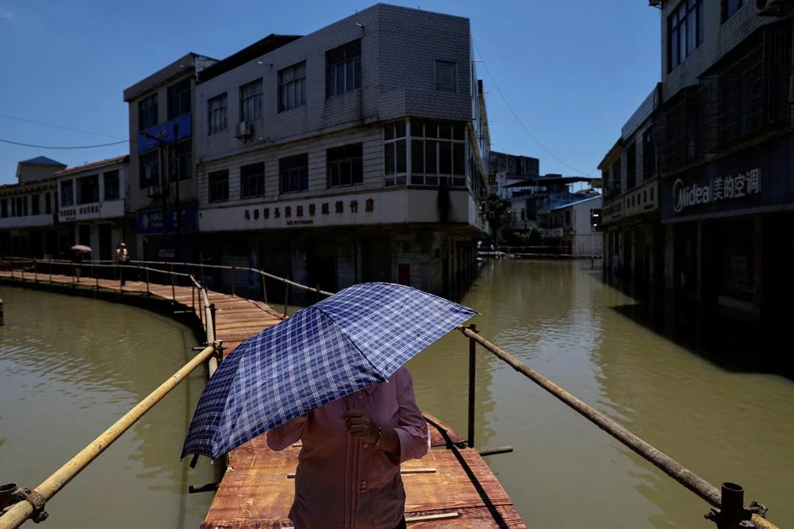 A resident holds an umbrella amid a yellow alert for heatwave, as she crosses a makeshift bridge following floods, in Hukou county, Jiujiang, Jiangxi province, on July 5.