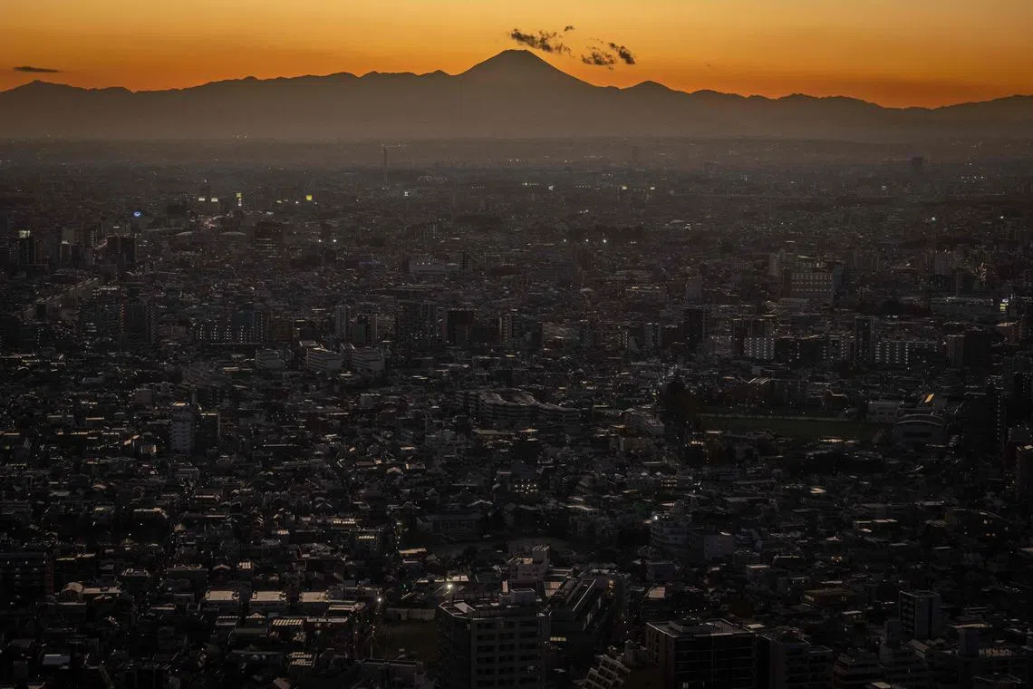 Mount Fuji (back) is seen behind the city skyline at dusk from Tokyo Metropolitan Government Building Observatories in Tokyo on December 15, 2022. 