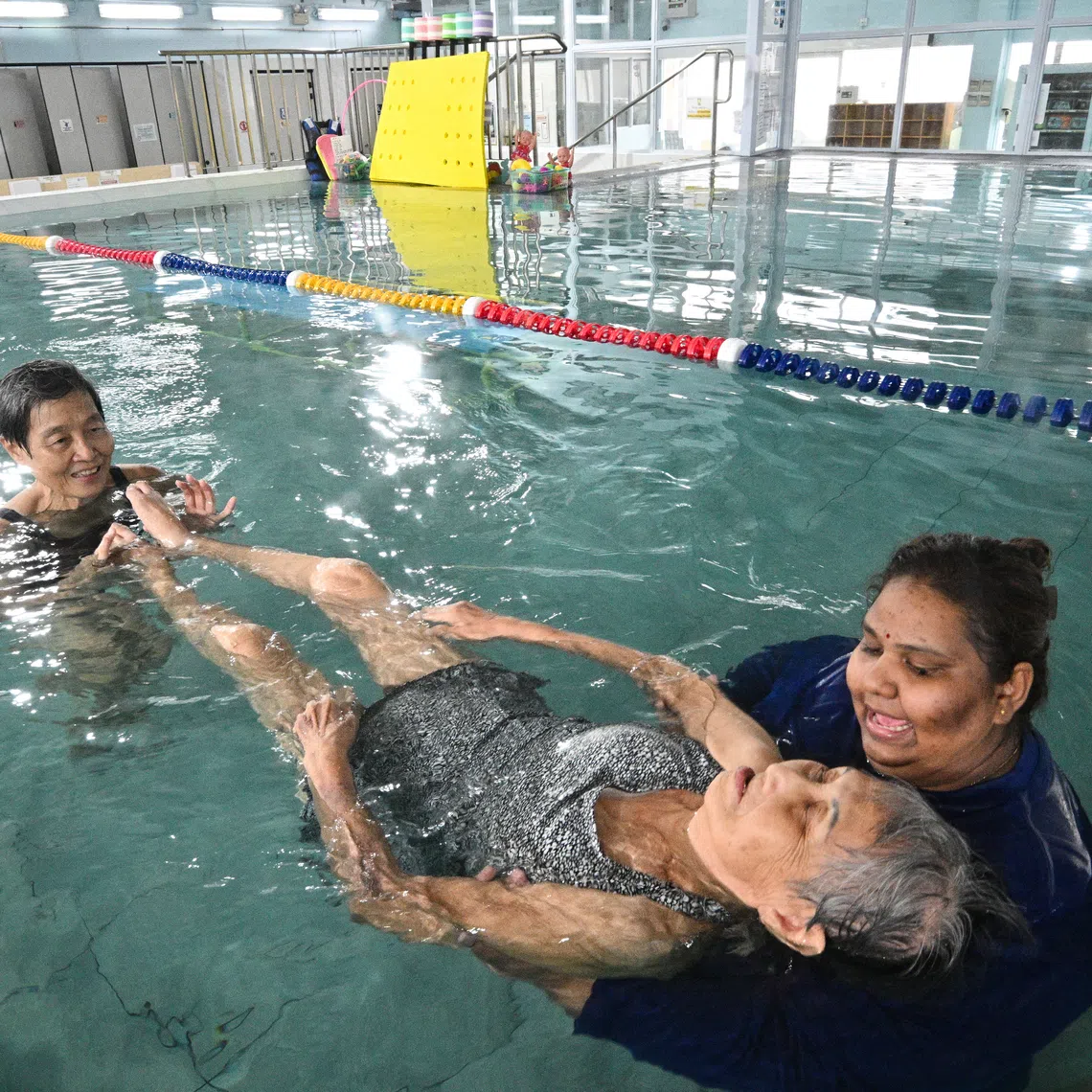 Madam Peggy Tan being supported by Ms Ananthy Murugan, while Ms Deborah Tan holds on to Peggy's legs during an adaptive physical disability class at Little Splashes @ Enabling Village on Oct 2.