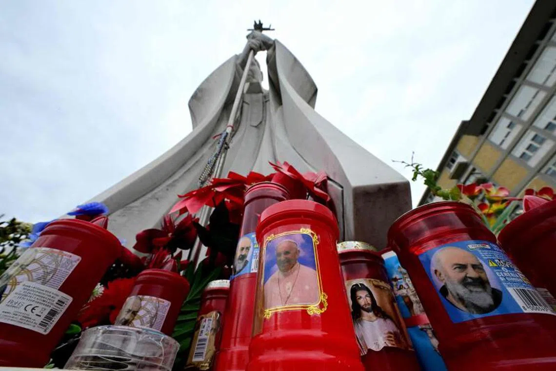 A candle with a portrait of Pope Francis is set at the bottom of a statue of Pope John Paul II at the Gemelli hospital where Pope Francis is hospitalised for tests and treatment for bronchitis, in Rome on February 17, 2025. Pope Francis, hospitalised for bronchitis four days ago, faces a “complex clinical picture” that will require the 88-year-old to stay longer than originally expected, the Vatican said on February 17, 2025. (Photo by Tiziana FABI / AFP)