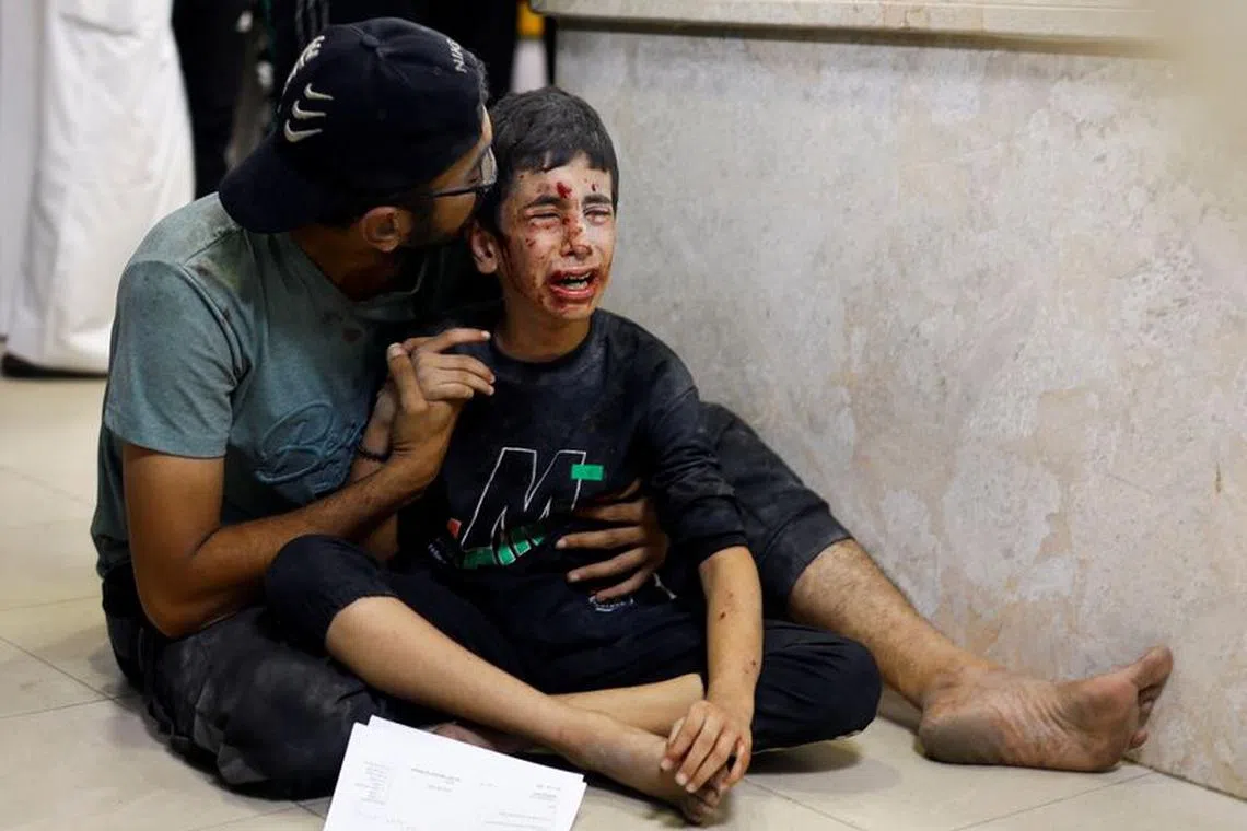 A Palestinian man sits with a child wounded in an Israeli strike at Nasser hospital, amid the ongoing conflict between Israel and Palestinian Islamist group Hamas, in Khan Younis in the southern Gaza Strip November 18, 2023. REUTERS/Mohammed Salem
