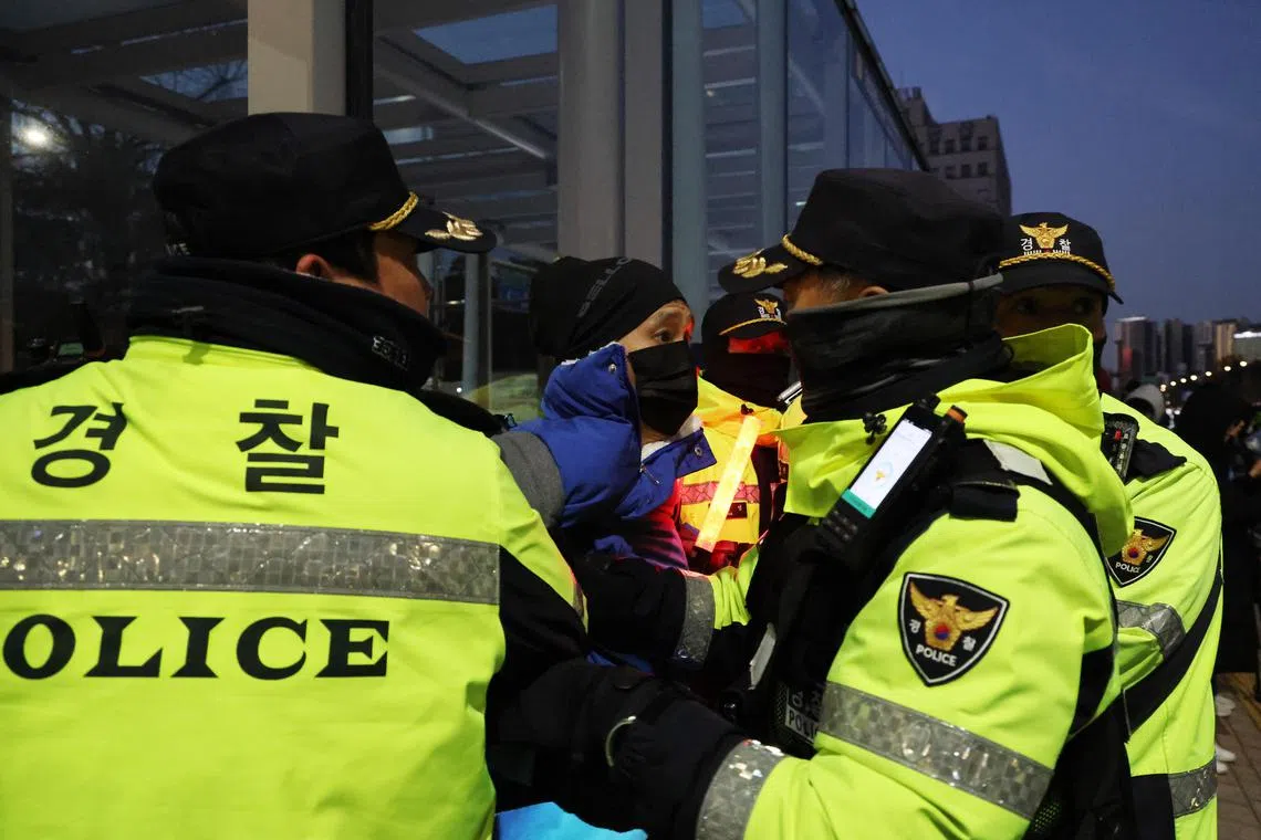 epa11755817 Police officers surround a protester outside the National Assembly after South Korean President Yoon Suk Yeol announced his intention to lift the emergency martial law in Seoul, South Korea, 04 December 2024. President Yoon annnounced his intention to lift the emergency martial law hours after the National Assembly unanimously voted in favor of a resolution urging the president to withdraw the martial law during an emergency plenary session. Yoon had declared martial law the previous night, citing the need to root out pro-North Korean forces and uphold the constitutional order.  EPA-EFE/HAN MYUNG-GU