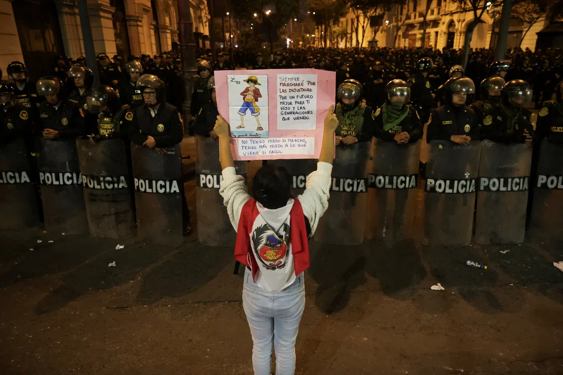 FILE PHOTO: A demonstrator holds a poster as police officers stand guard during a protest against the government of Peru's President Dina Boluarte after Congress approved a partial withdrawal of private pension savings, a measure which could leave millions of Peruvians without retirement funds, in Lima, Peru, September 20, 2025. REUTERS/Sebastian Castaneda/File Photo