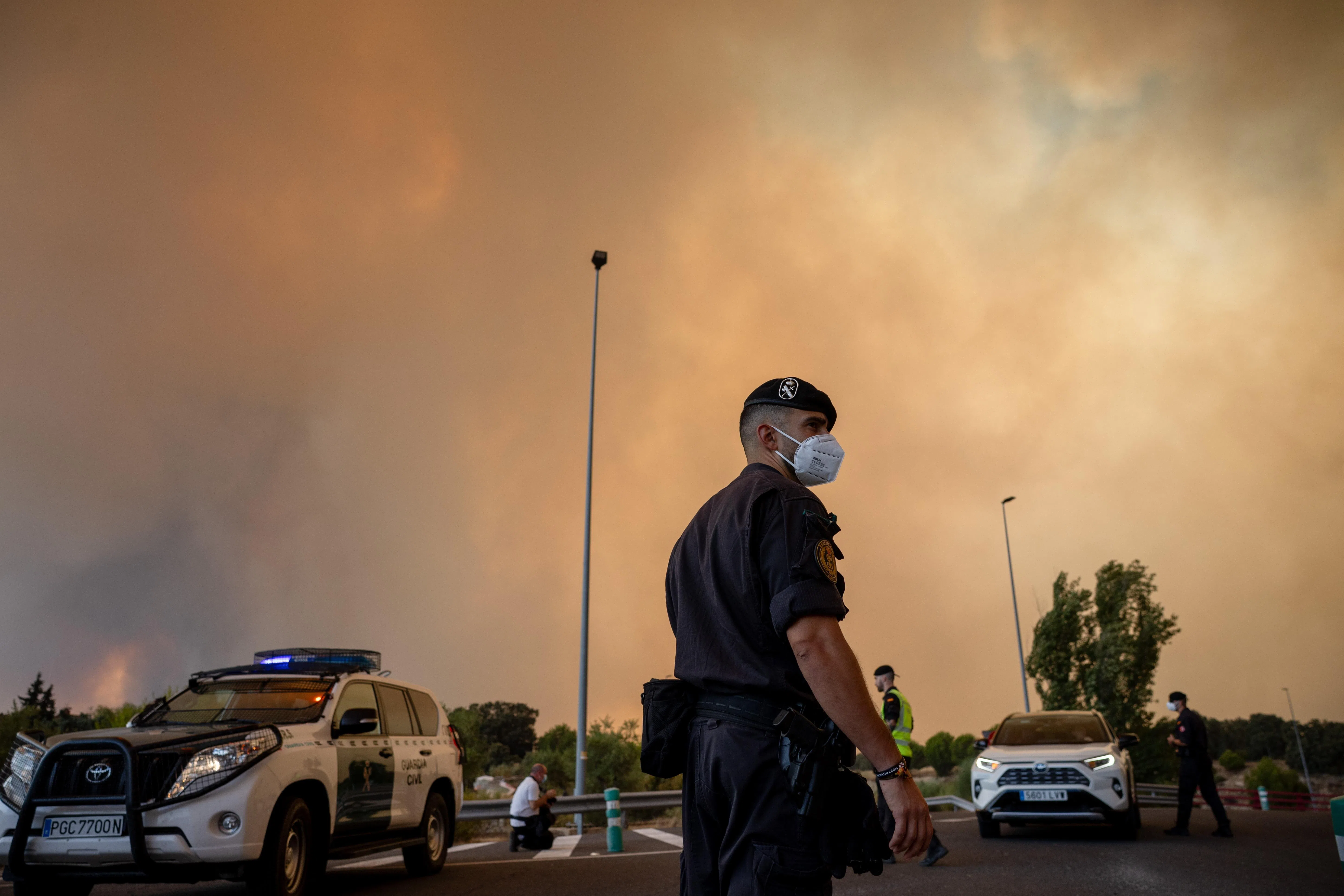 epa13130572 A Civil Guard officer wears a protective mask as smoke from a wildfire obscures the sky in Cenicientos, Madrid, Spain, 24 July 2026. Forest fires that broke out in Almorox (Toledo province) and San Martín de Valdeiglesias (Madrid) have merged into a single front, spreading uncontrollably due to adverse weather conditions, forcing the evacuation of three municipalities in Madrid.  EPA/Daniel Gonzalez