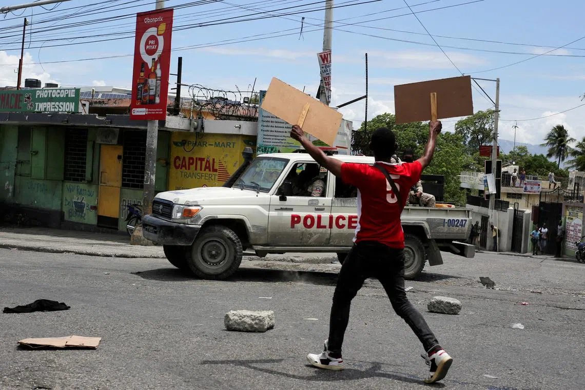 FILE PHOTO: A man holds up placards as he yells toward a patrol car during a protest against gang-related violence and to demand the resignation of Haiti's transitional presidential council, in Port-au-Prince, Haiti, May 15, 2025. REUTERS/Jean Feguens Regala/File Photo