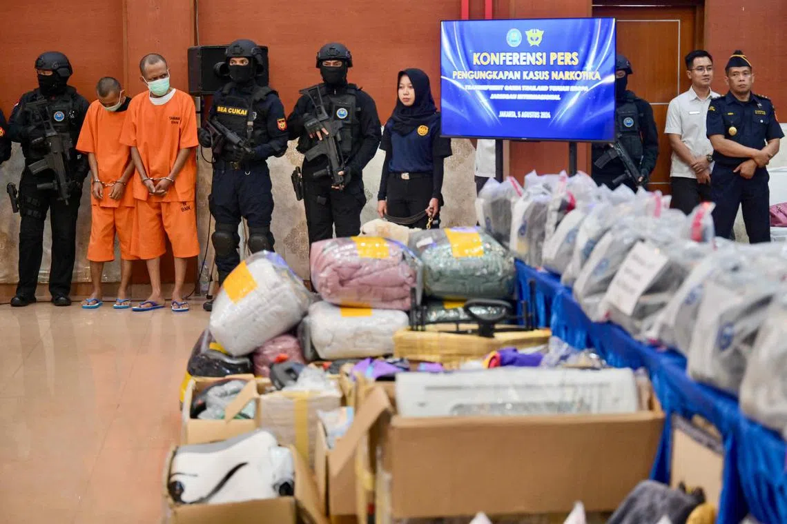 Armed officers from Indonesia's National Narcotics Agency guard two suspects during a press conference on the uncovering of an international network that smuggled marijuana to Britain from Thailand and via Indonesia, in Jakarta on August 5, 2024. The two suspects were arrested over accusations of owning a company that had received 214 packages of bed covers containing hidden marijuana weighing 113.65 kilograms and valued at 25 billion Indonesian Rupiah (approximately  1.6 million USD). (Photo by BAY ISMOYO / AFP)