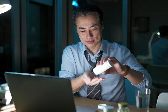 A middle-aged man taking supplements after working late in the office