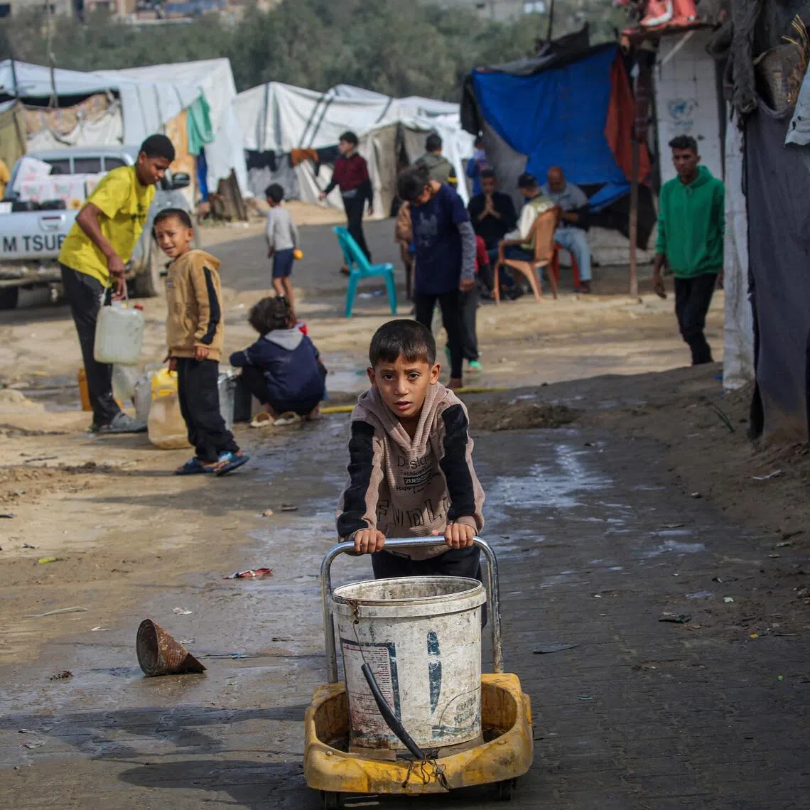 A boy pushes a bucket as children fill their containers with water at the Nuseirat camp for displaced Palestinians in central Gaza.
