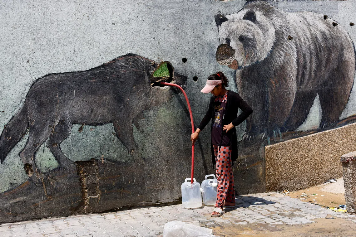 A Palestinian girl fills water containers outside the wall of a zoo damaged during the war, in Gaza City, August 15, 2026. REUTERS/Mahmoud Issa     TPX IMAGES OF THE DAY