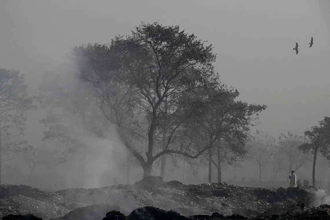 A man walking past burning garbage along a roadside amid dense smog in Lahore, on Dec 1, 2025. 