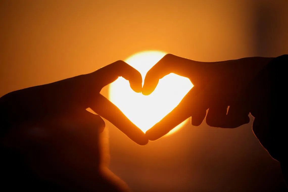 People make a heart-shaped gesture as they look at the first sunrise of the year at a park in Seoul, South Korea, on Jan 1, 2023. 
