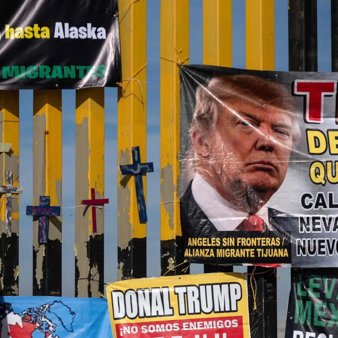 Crosses and protest banners depicting US President Donald Trump hang on the Mexico side of the Mexico–US border wall.