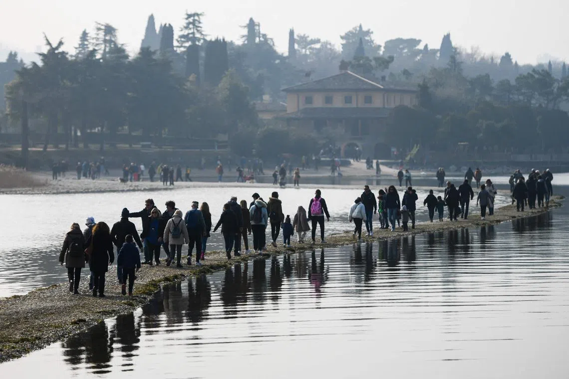 People walk from the small island of San Biagio, off Manerba del Garda, Lake Garda, towards the Belvedere point (Rear) on Feb 21, 2023, where the water level dropped to its lowest in 30 years during the winter months. - A lack of snow on the surrounding mountain peaks, the absence of rain for the past six weeks, and mild temperatures - this explosive cocktail has caused the water level of Italy's largest lake to drop to its lowest in 30 years during the winter months. 