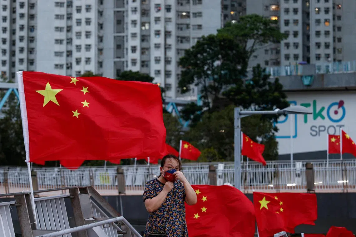 A pro-China supporter adjusts her protective mask near Chinese national flags ahead of Chinese National Day, in Hong Kong, China September 29, 2022. REUTERS/Tyrone Siu