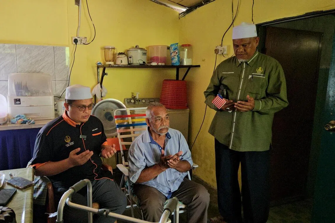 Northern Perak PAS assemblyman Akmal Kamarudin (left) and his right-hand man Ahmad Bakhtier Muslim (right, green shirt) offering a prayer during a pre-Independence Day appreciation visit in Selama, Perak on Aug 22.