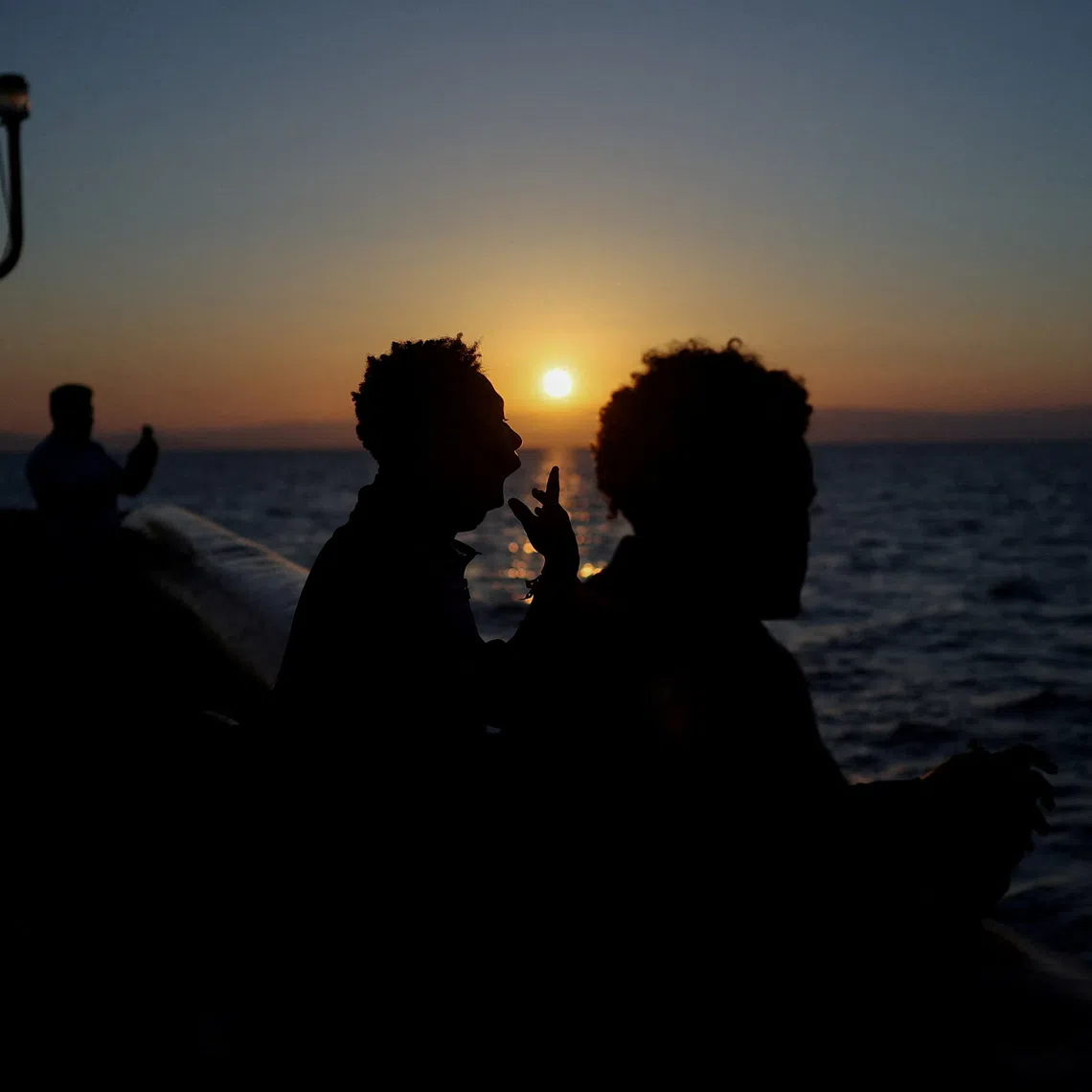 Migrants rescued two days earlier are silhouetted at dawn aboard the Ocean Viking as it sails toward Salerno, Italy, September 10, 2026. REUTERS/Stephane Mahe