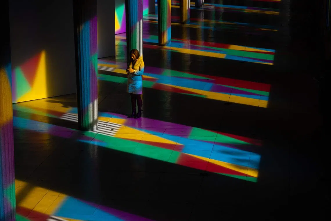A visitor using her smartphone next to the columns of “Allegro, ma non troppo”, a work by French visual artist Daniel Buren, enlightened in colours by the sun shining through multicoloured stained glass, at the Palais d'Iena in Paris on October 17, 2023. On the occasion of the 2023 Modern Art Fair's opening, planned for October 18, 2023, Daniel Buren transformed the windows of the Palais d'Iena into multicoloured stained glass to fill the place in colours with the sun's light. 