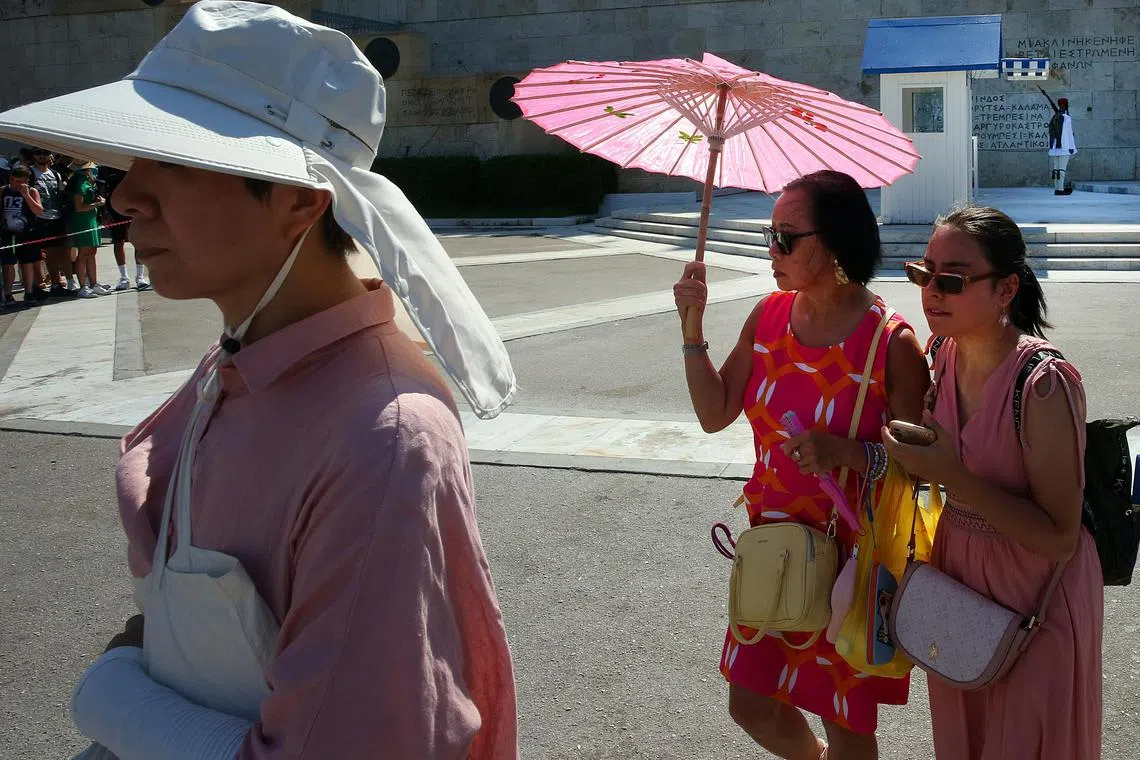 Tourists wear hats and use fans and umbrellas as they stroll in the city centre during a heatwave in Athens, Greece.