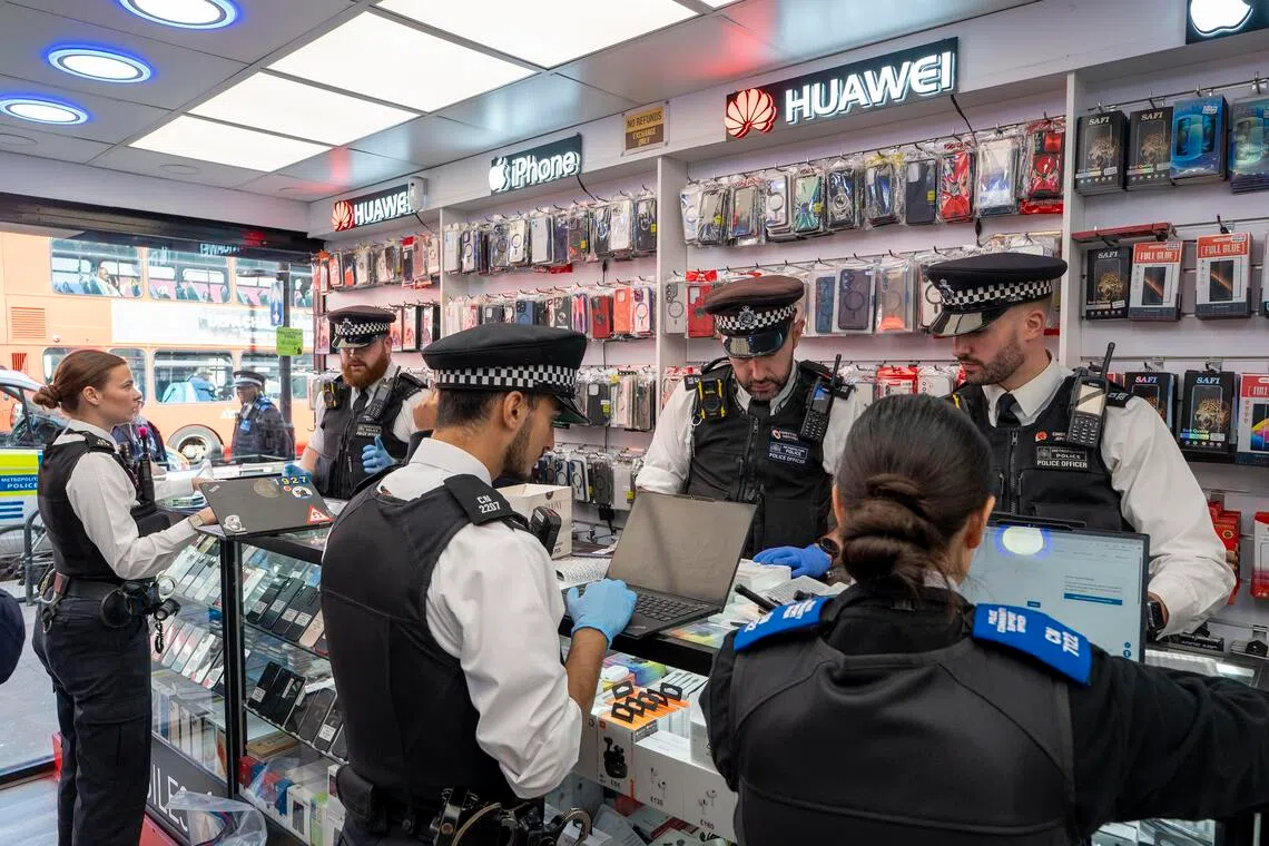 Police officers searching a secondhand phone shop in north London on Sept. 25.